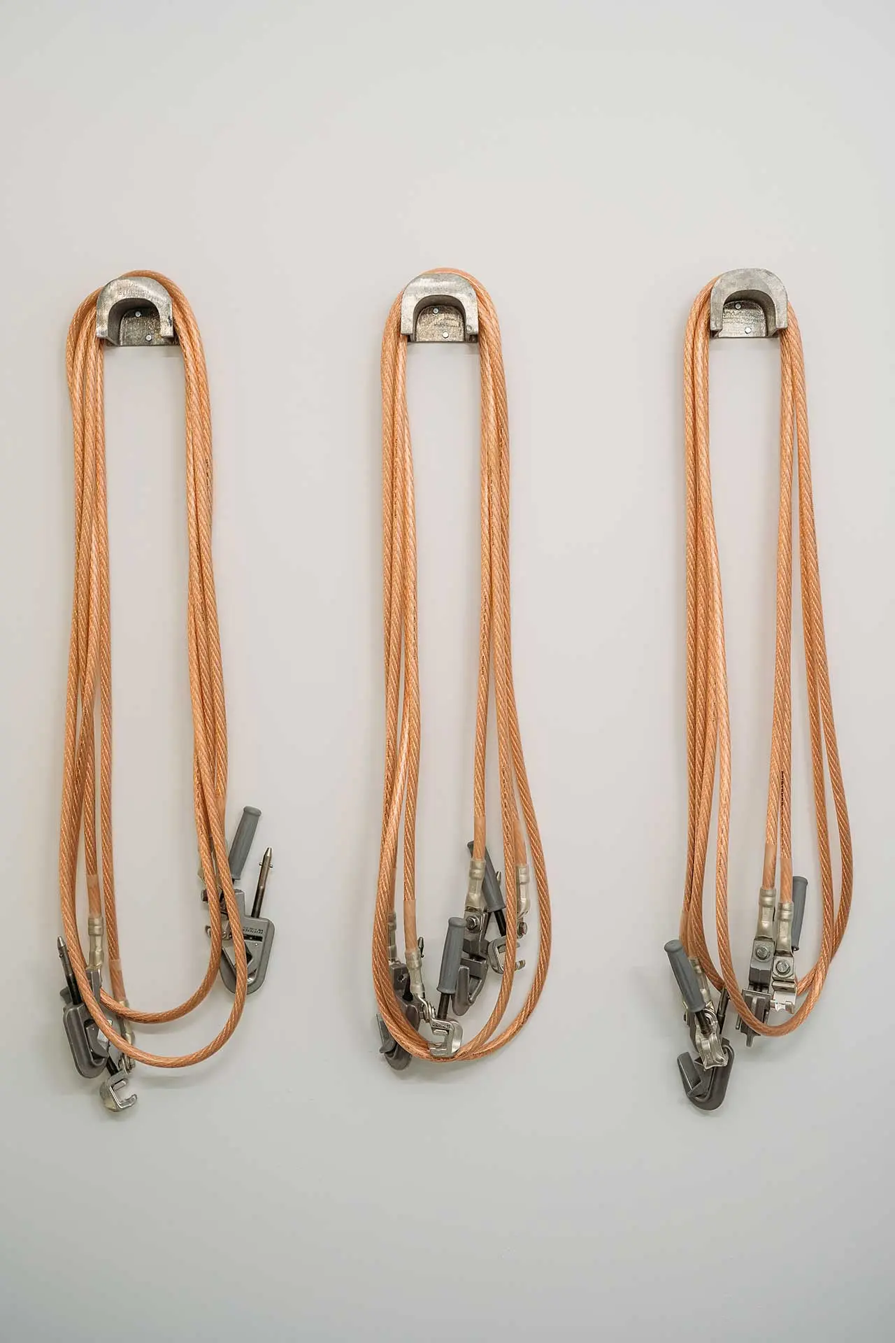 Drei orangefarbene Kletterseile mit Metallbeschlägen hängen an einer Wand.