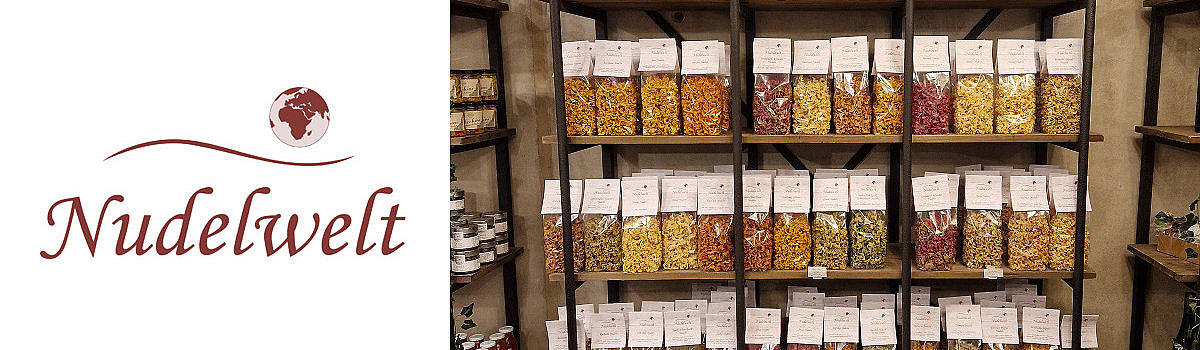 Alt-Tag: Bunte Pastavariationen in durchsichtigen Tüten auf Regalen im Geschäft Nudelwelt.