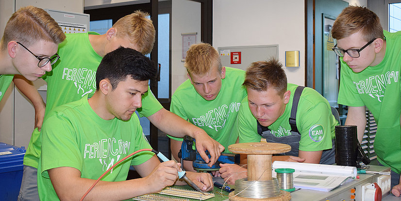Sechs Jugendliche in grünen T-Shirts arbeiten gemeinsam an einem Projekt im technischen Bereich.