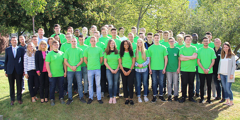 Gruppenshot von Personen in grünen T-Shirts, die im Freien zusammenstehen, umgeben von Bäumen und Rasen.