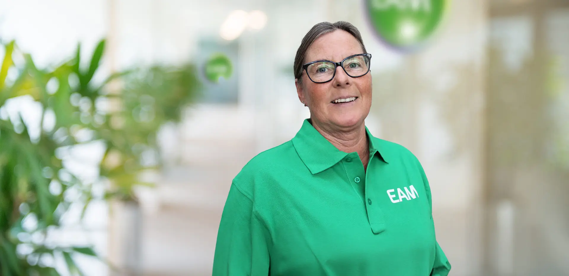 Eine lachende Frau steht vor einem EAM-Logo in einem Büro.