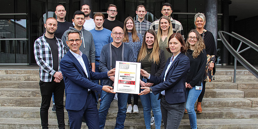 Gruppe von Menschen steht auf einer Treppe und hält eine Auszeichnung für Deutschlands beste Ausbildungsbetriebe.