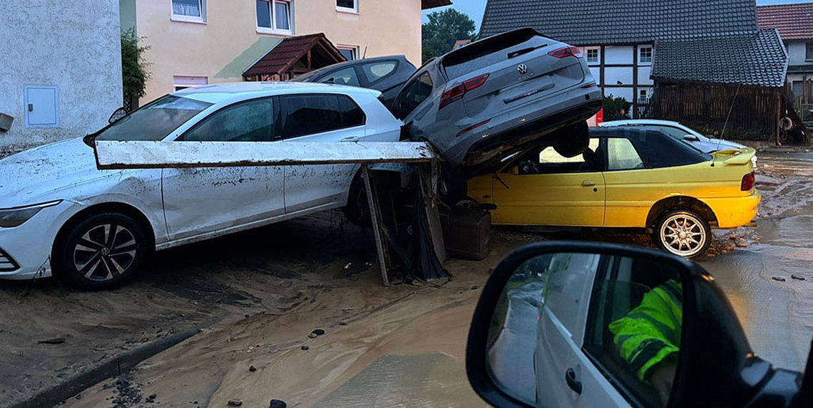 Stark beschädigte Autos, darunter ein weißer und ein grauer Pkw, sind nach einem Unwetter auf Trümmern und einem gelben Cabrio gestapelt.