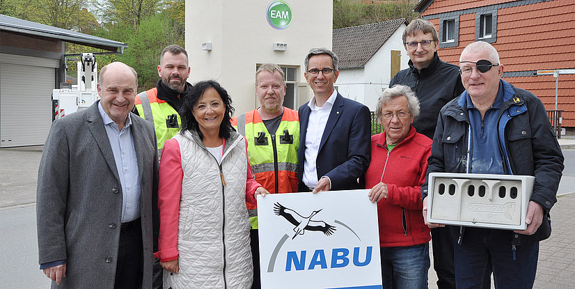 Gruppenszene mit Menschen, die ein NABU-Schild halten und ein Produkt präsentieren, im Freien vor einem Gebäude.