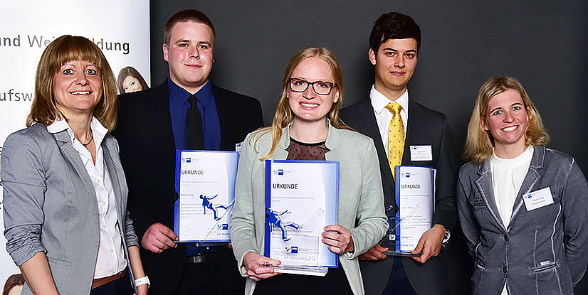 Gruppiertes Foto von fünf Personen mit Zertifikaten, die stolz lächeln und an einer Preisverleihung teilnehmen.
