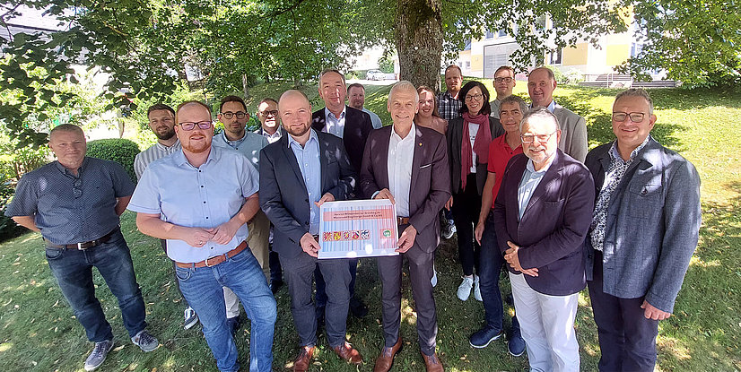 Gruppenfoto von Personengruppe im Freien, einige halten ein Schild mit den Farben und Wappen von Unternehmen und Organisationen.