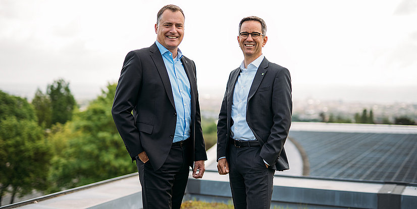 Die EAM-Geschäftsführer Olaf Kieser und Hans-Hinrich Schriever stehen auf dem Dach eines Gebäudes, im Hintergrund Solarmodule und grüne Bäume..