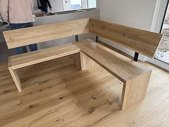 L-förmige Sitzecke aus Holz mit Rückenlehne, auf einem Holzboden in einem modernen Raum.