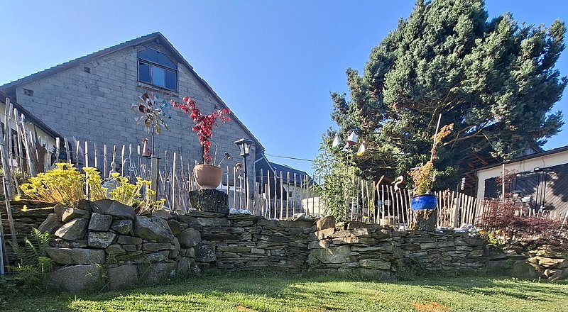 Ein mehrstöckiger Garten mit bunten Pflanzen, geschmackvoller Steinmauer und einem Haus im Hintergrund unter klarem Himmel.