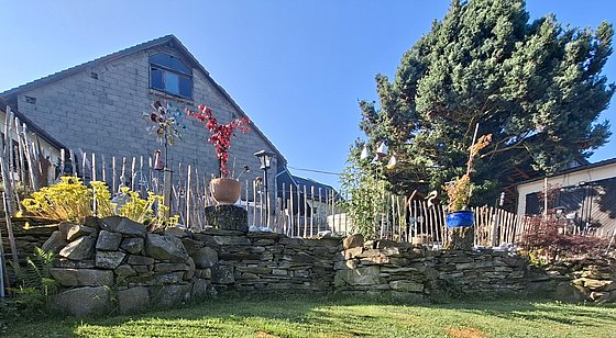Ein mehrstöckiger Garten mit bunten Pflanzen, geschmackvoller Steinmauer und einem Haus im Hintergrund unter klarem Himmel.