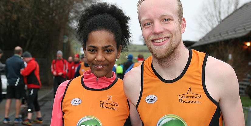 Zwei Läufer, eine Frau und ein Mann, posieren nach einem Rennen im Freien, die Frau trägt eine Medaille.