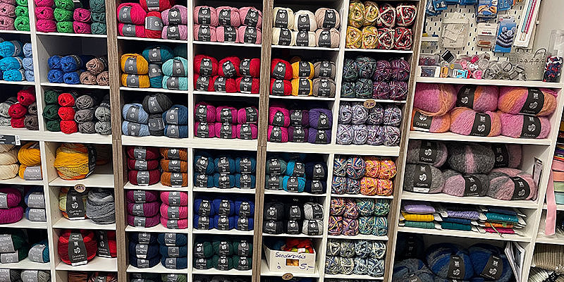 Bunte Wollknäuel auf Regalen, sortiert nach Farbe, in einem Handarbeitsgeschäft.