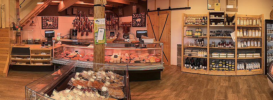 Blick in einen Lebensmittelgeschäft mit Fleischtheke, Holzregalen und variierter Produktauslage.