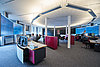 Netzleittechnik Büro mit mehreren Arbeitsplätzen, großen Monitoren und modernen Möbeln, Personen arbeiten an Computern.