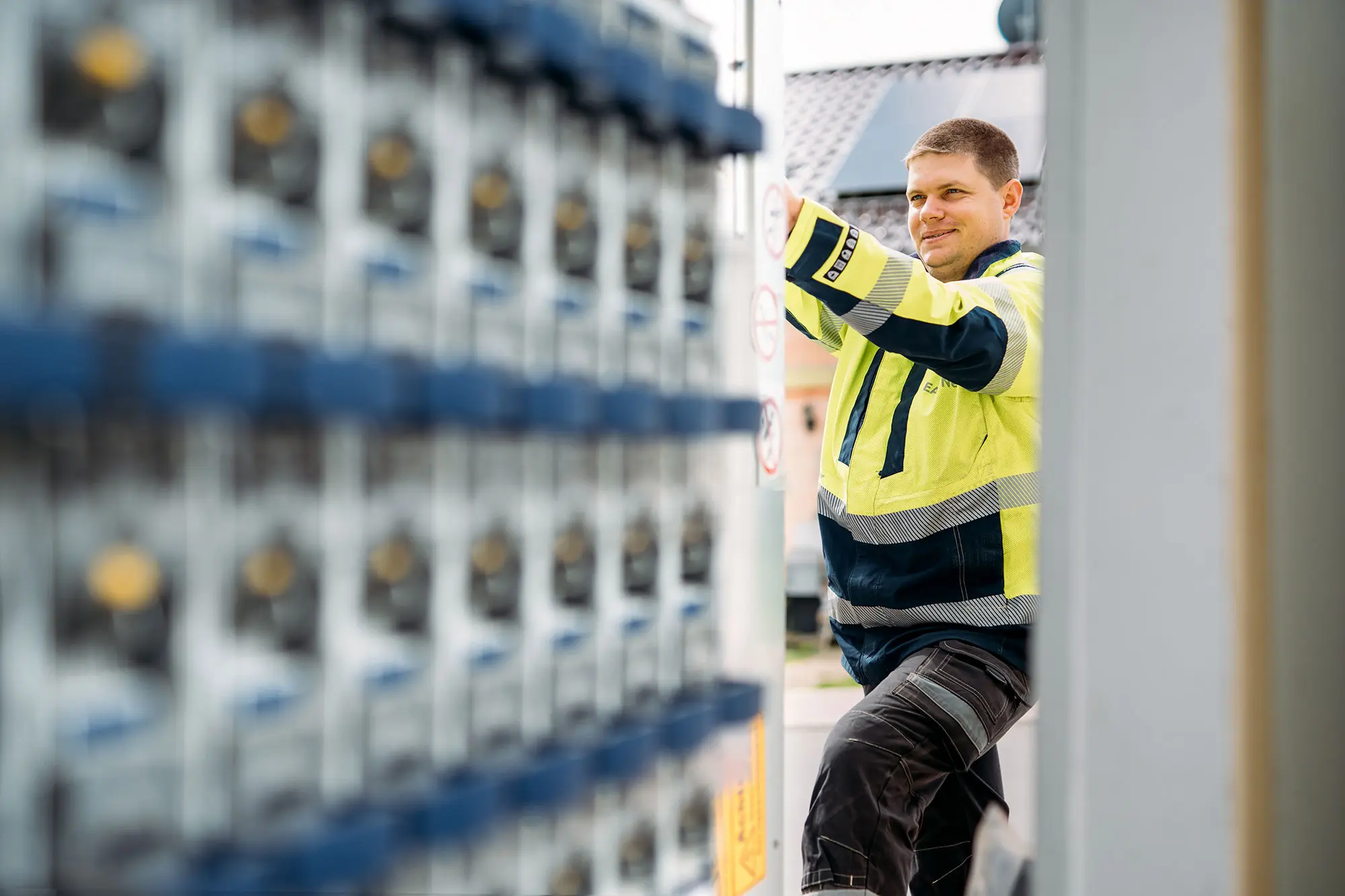 Ein EAM-Mitarbeiter in gelber Warnschutzjacke arbeitet an einer geöffneten technischen Anlage; links im Vordergrund sind unscharf Stromzähler zu sehen.
