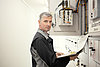 Betriebsführung von Niederspannungs- und Mittelspannungsanlagen Techniker mit einem Dokument in der Hand, arbeitet an einem elektrischen Schaltschrank in einem technischen Raum.