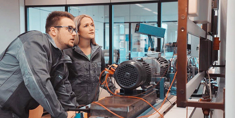 Ein Mann und eine Frau, blicken konzentriert auf eine Industriemaschine in einem Labor oder Werkstatt.