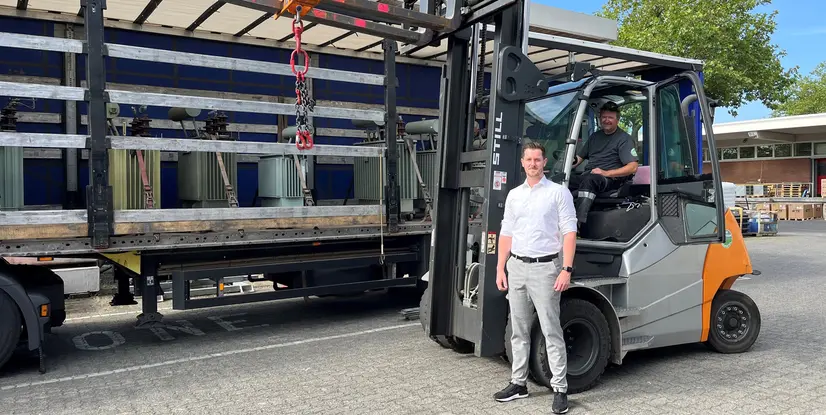 Ein Mann steht neben einem Gabelstapler, während ein Fahrer im Fahrzeug sitzt, im Hintergrund sind Paletten und einen Transporter sichtbar.