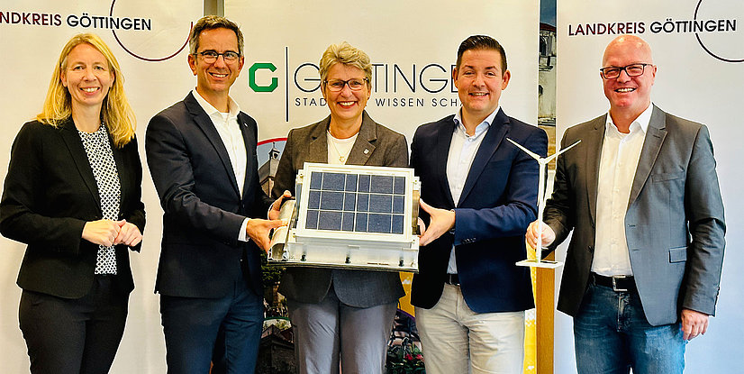 Eine Gruppe von Personen hält ein Solarmodul und ein Modell einer Windkraftanlage, im Hintergrund Logos von Göttingen.