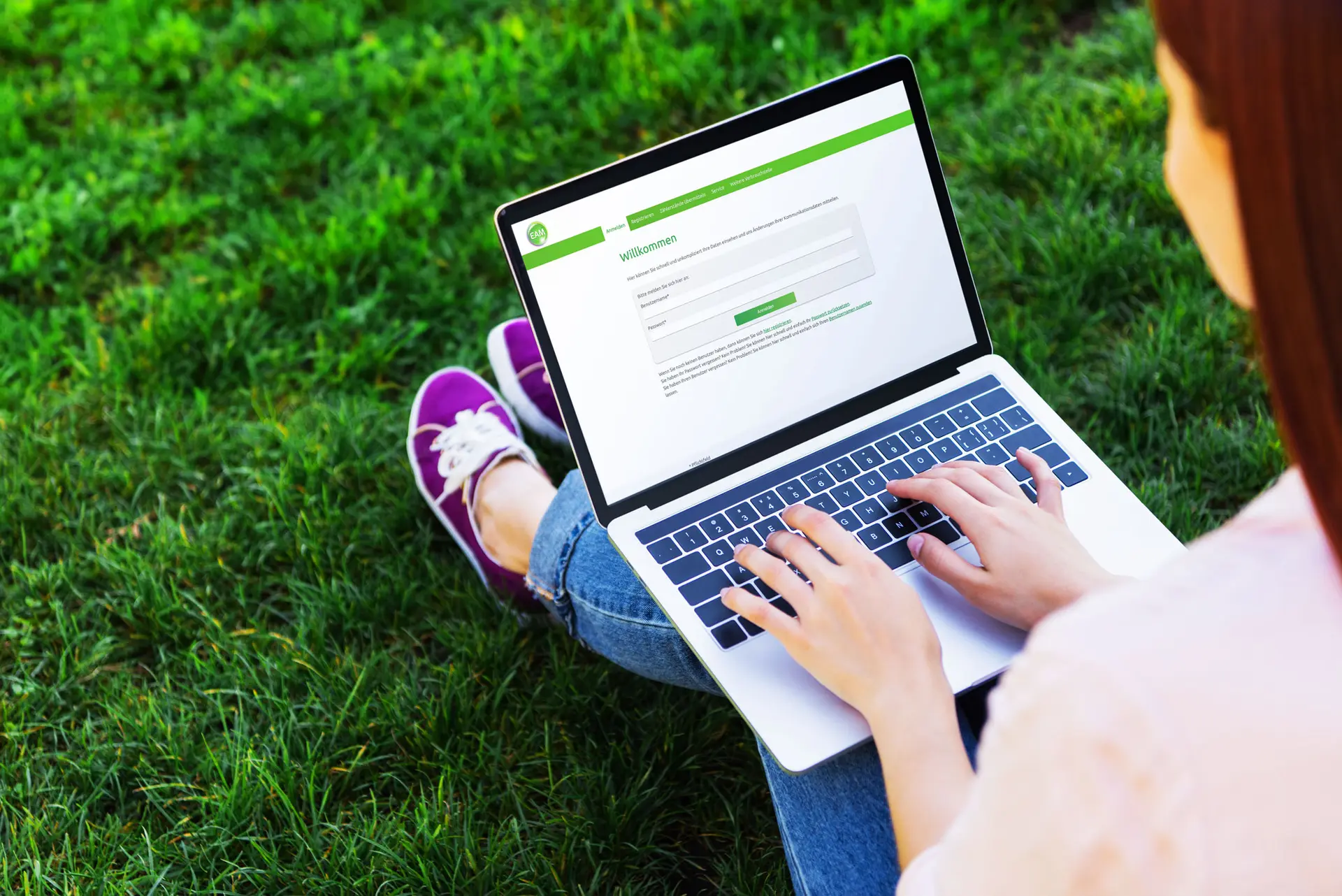 Eine Person tippt auf einem Laptop mit der EAM-Webseite auf dem Bildschirm, sitzend auf Gras