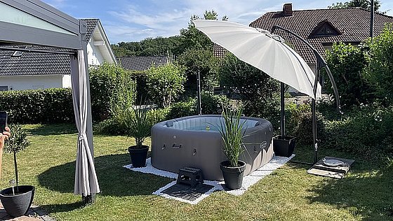Ein aufblasbarer Whirlpool im Garten, umgeben von Pflanzen und einem Sonnenschirm.