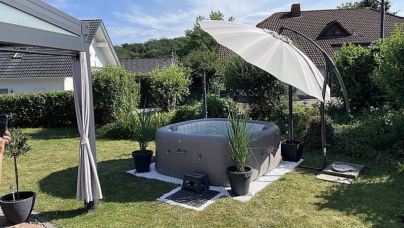 Ein aufblasbarer Whirlpool im Garten, umgeben von Pflanzen und einem Sonnenschirm.