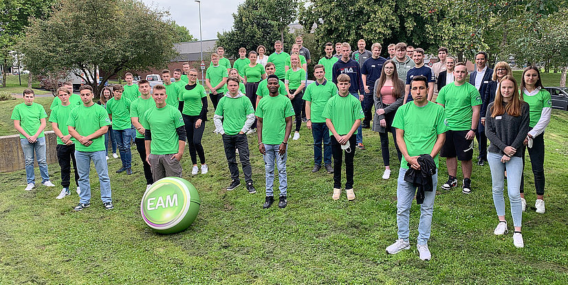 Gruppenbild der neuen Auszubildenden in grünen T-Shirts vor einem Baum, mit einem großen grünen Ball mit EAM-Logo im Vordergrund.