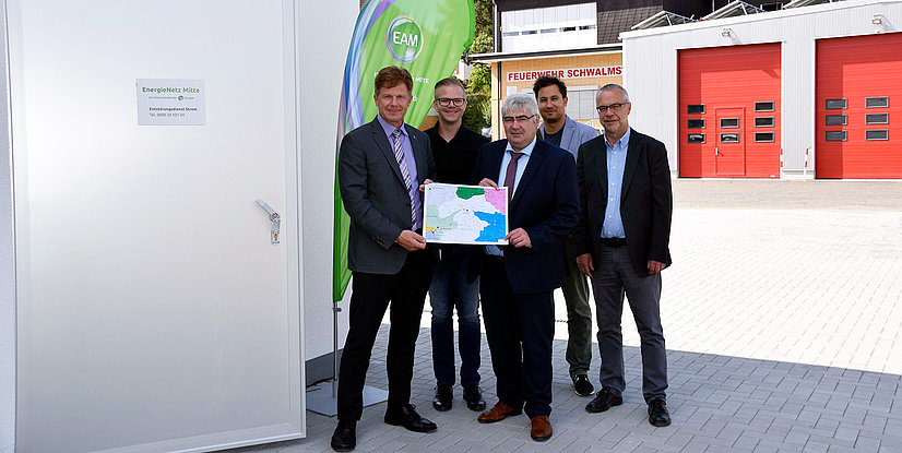 Fünf Personen präsentieren eine Karte vor einem Gebäude, gekennzeichnet mit EnergieNetz Mitte