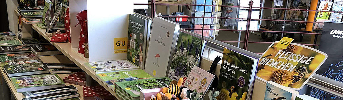 Bunte Buchausstellung mit Garten- und Pflanzenliteratur, dekoriert mit Pflanzen und Kitsch-Elementen.