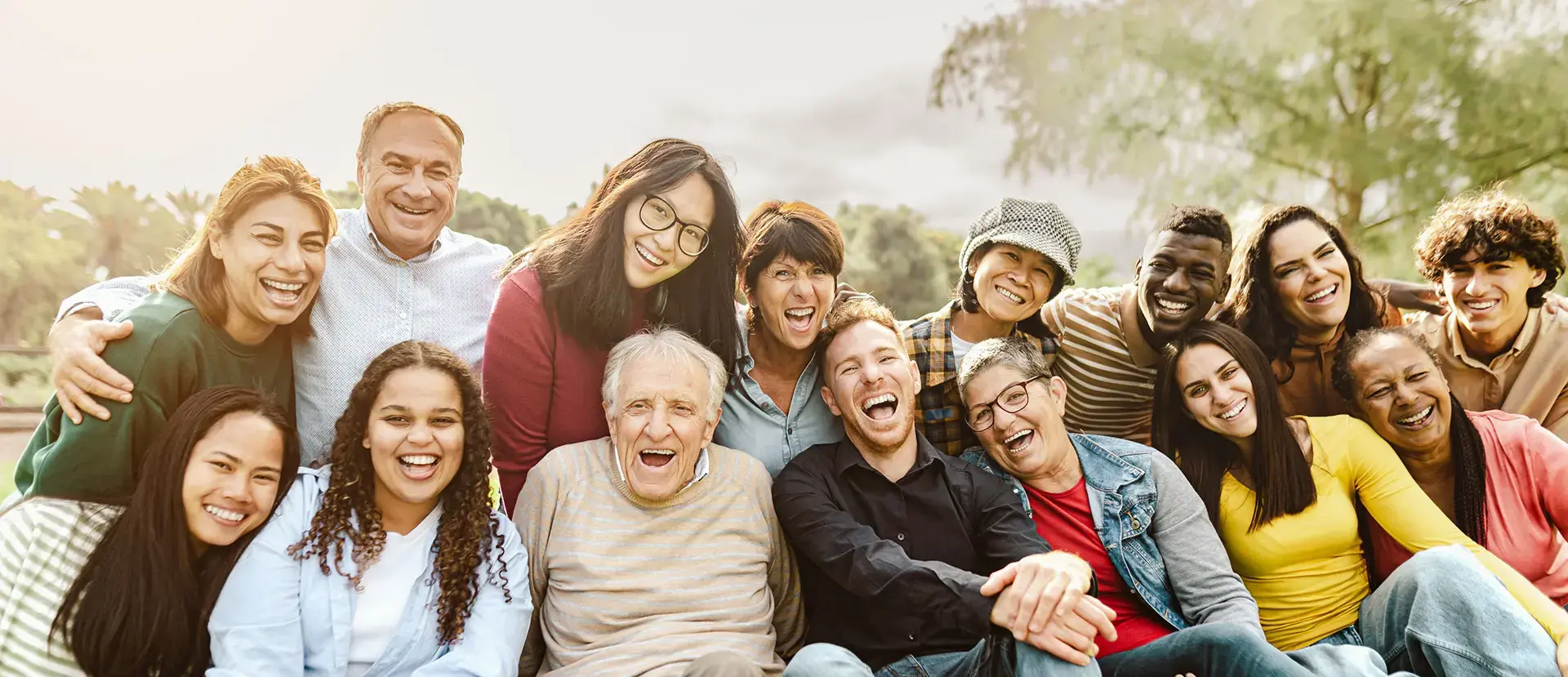 Gruppe diverser Menschen unterschiedlichen Alters, die eng zusammenstehen, lachen und in die Kamera schauen.