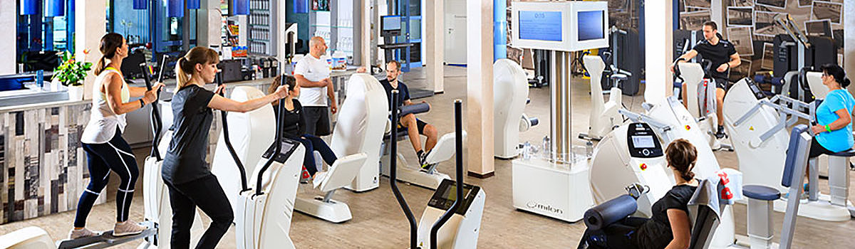 Fitnessstudio mit mehreren Personen, die verschiedene Trainingsgeräte nutzen, in einem hellen und modernen Raum.