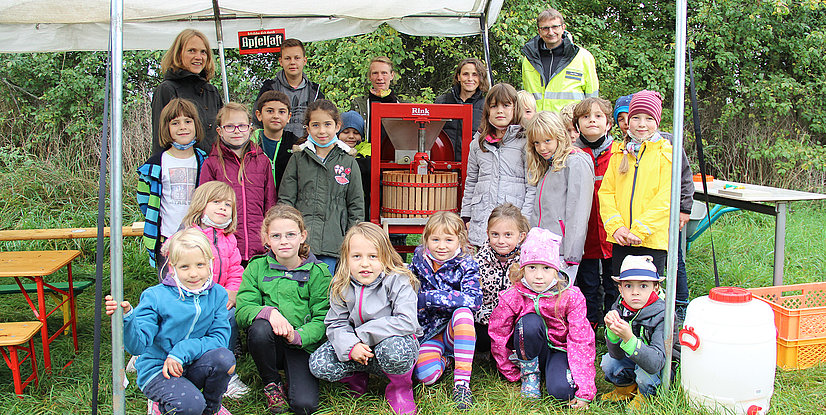  Ein Gruppe von Kindern und einigen Erwachsenen posiert vor einem Zelt mit einer Apfelpresse.