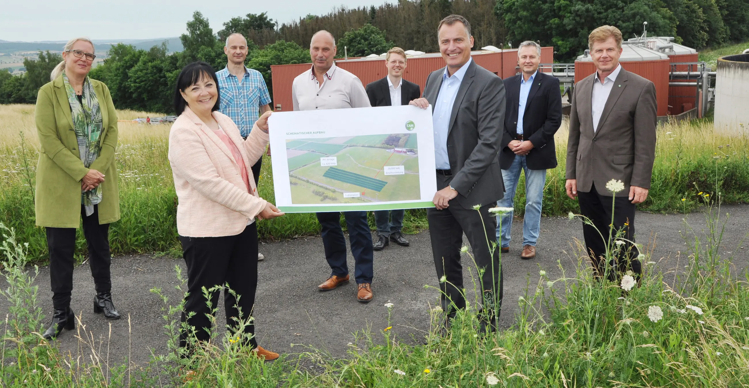 Gruppenfoto im Freien zur Vorstellung eines Plans für eine landwirtschaftliche Fläche mit Farbschema und Beschriftungen.
