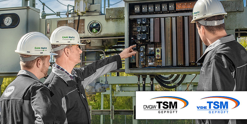 Drei Techniker mit Helmen analysieren elektrische Schaltanlagen in einem Umspannwerk. EAM Netz Logo sichtbar.