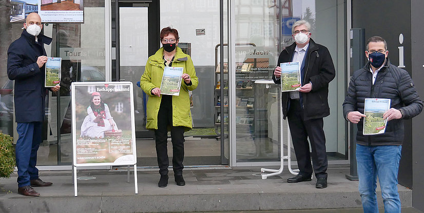 Vier Personen stehen vor einer Touristeninformation, halten Broschüren. Plakat für Rotkäppchenland im Hintergrund.