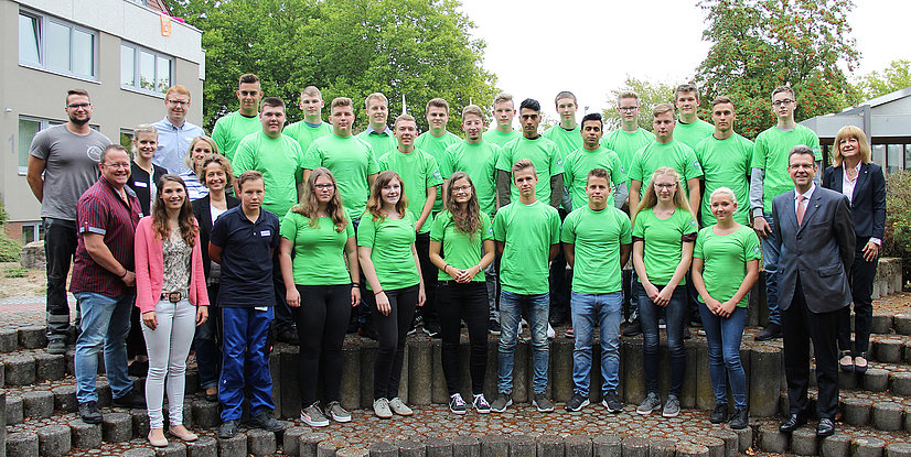 Gruppe von Personen in grünen T-Shirts steht auf einer Treppe im Freien, umgeben von Bäumen und Gebäuden.