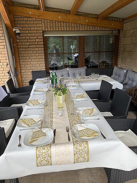Elegant gedeckter Tisch für eine festliche Mahlzeit im Freien, umgeben von bequemen Stühlen und Fenstern.