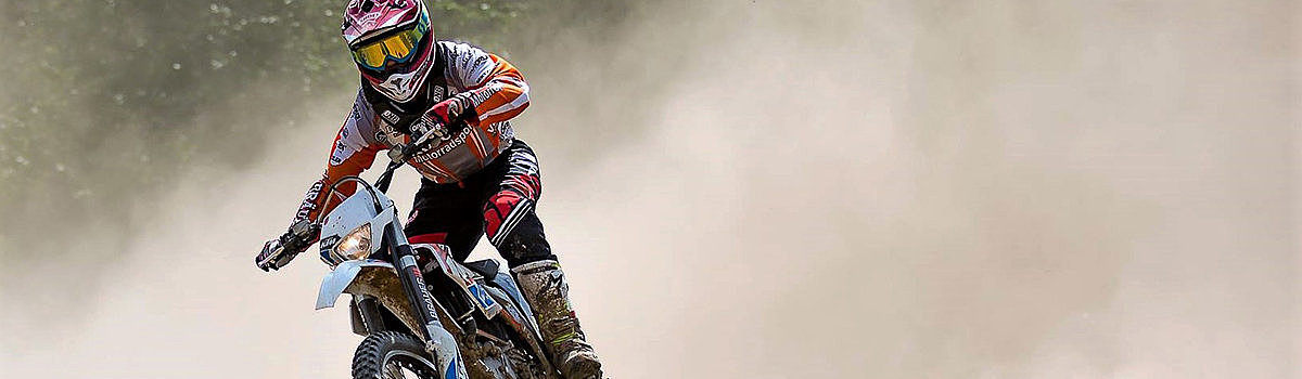 Motorradfahrer auf einer staubigen Strecke, der beim Offroad-Fahren eine Kurve nimmt.