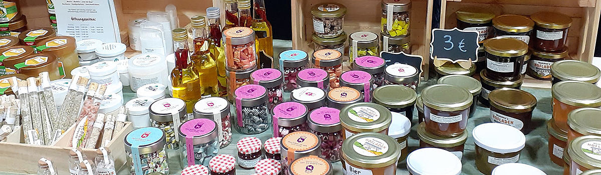 Vielfältige Produkte in Gläsern, darunter Marmeladen, Honig und Öle, aus einem regionalen Laden auf einem Markt.