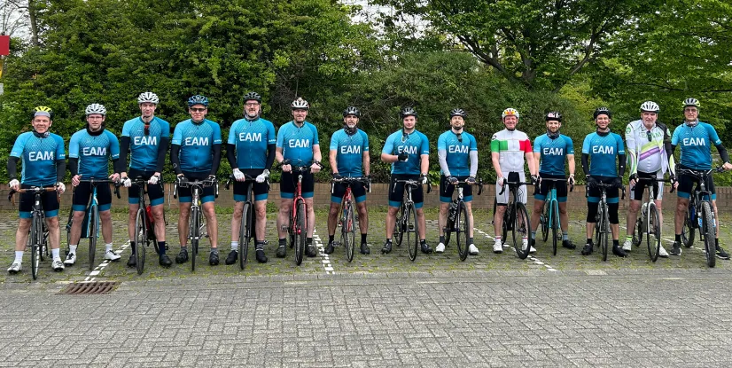 Gruppe von Radfahrern in blauer Teamsportkleidung, stehend neben ihren Fahrrädern, lächelnd in einer natürlichen Umgebung.