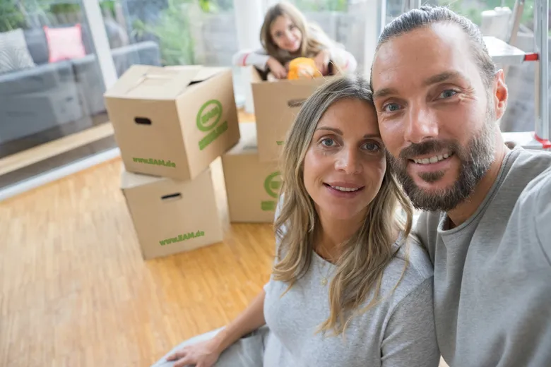 Familie posiert für ein Selfie vor Umzugskisten in einem hellen, modernen Raum.