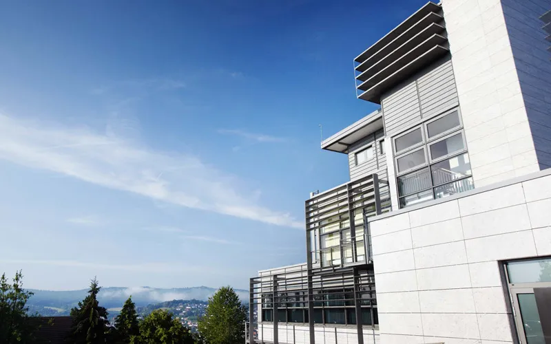 Modernes Gebäude mit Glasfassade und umliegender Landschaft unter blauem Himmel.