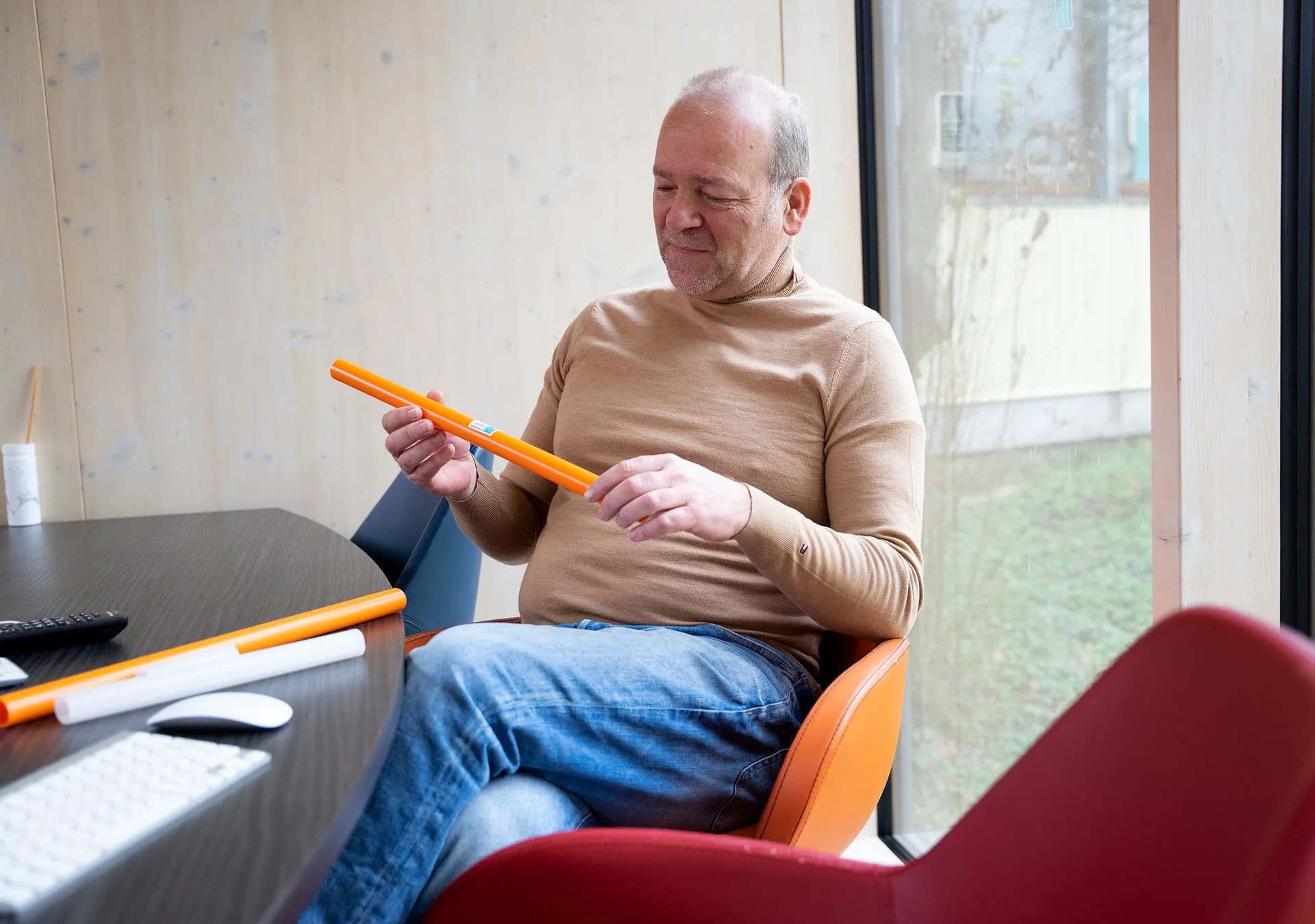 Mann sitzt an einem Tisch und hält zwei orangefarbene Stäbe, während er auf einen Bildschirm schaut.