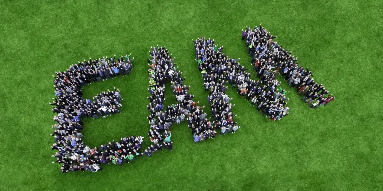 Eine große Gruppe von Menschen bildet das Wort "EAM"" auf einer grünen Wiese."
