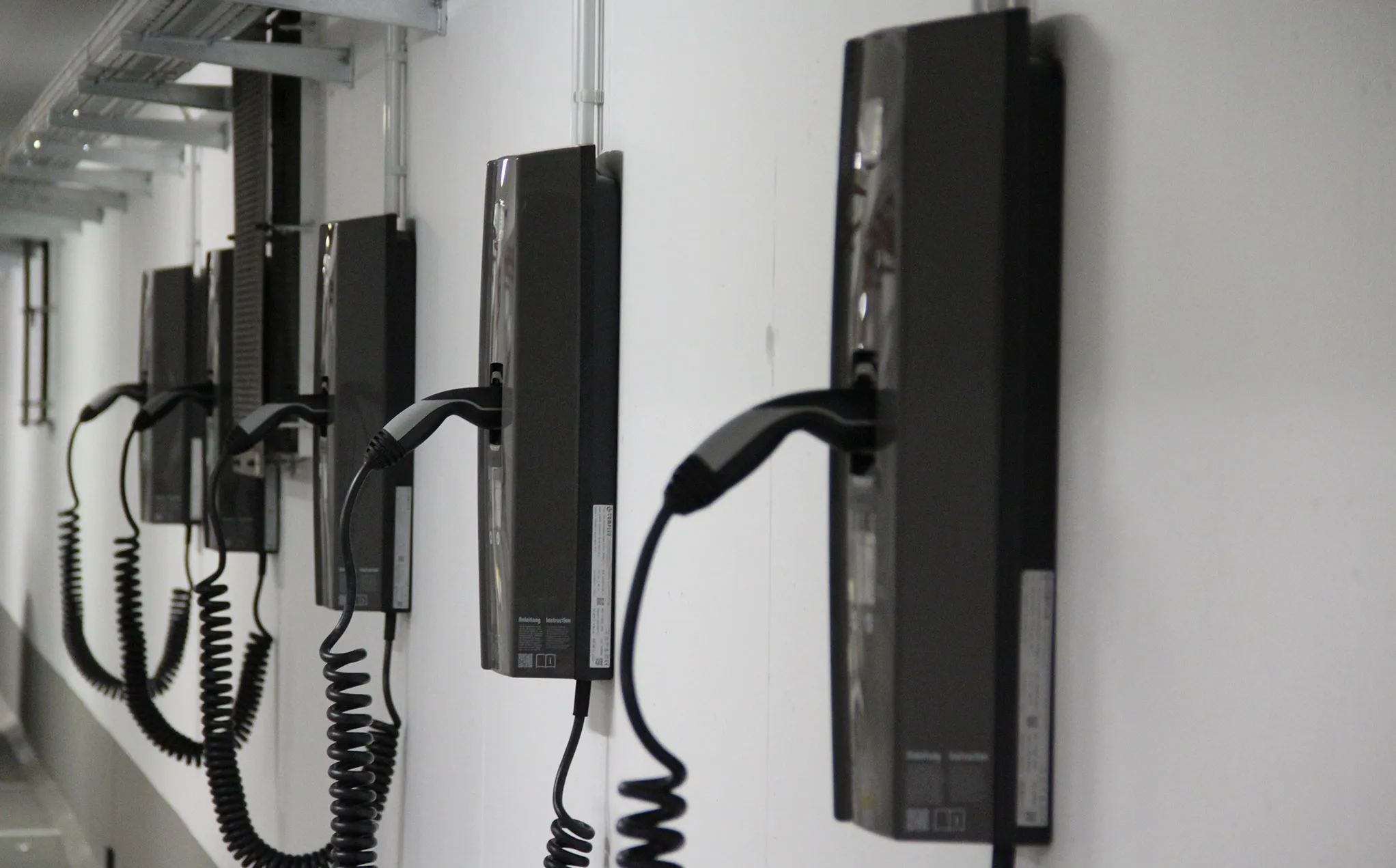 Mehrere schwarze E-Ladesäulen hängen an einer weißen Wand.