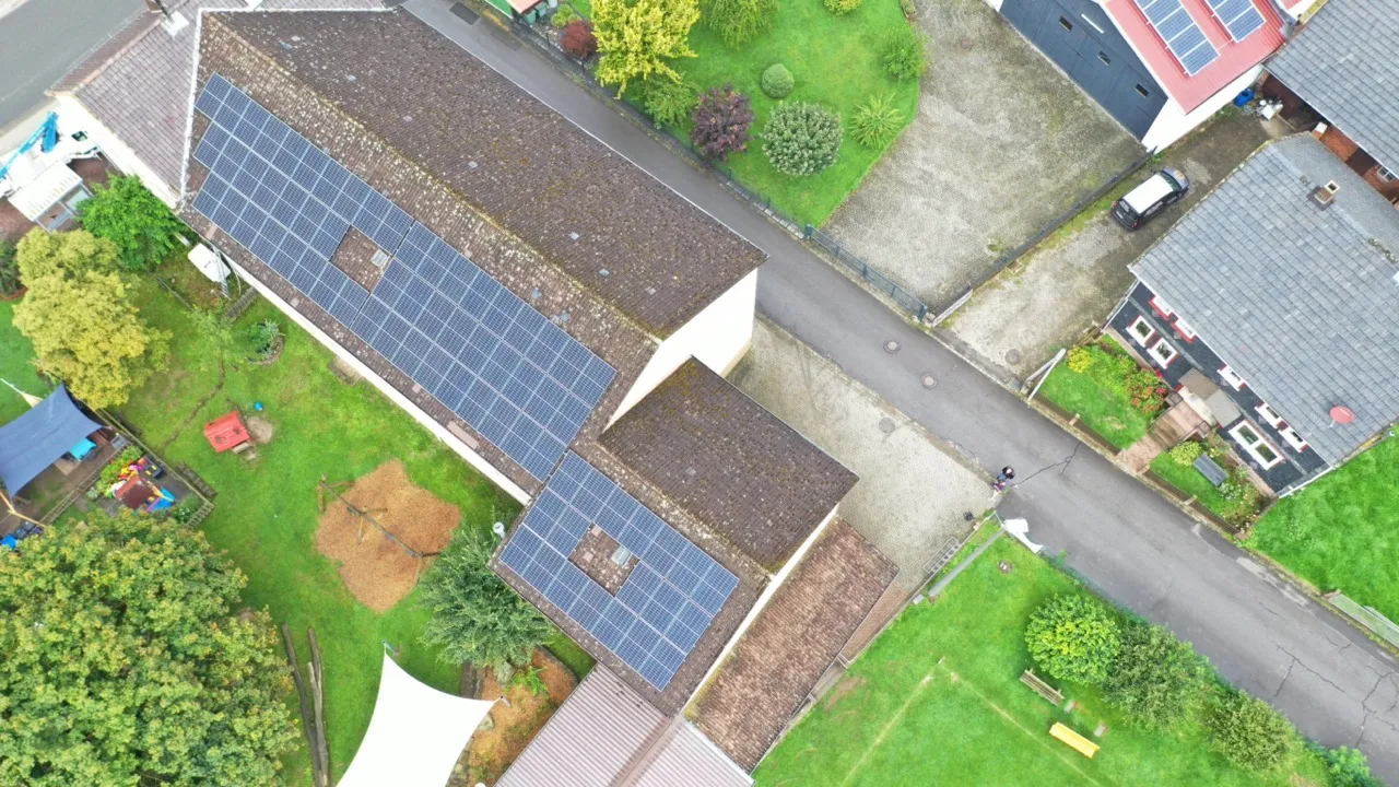 Luftaufnahme von einem Dach eines Einfamilienhauses das auf einer Seite mit PV-Anlagen ausgestattet ist.