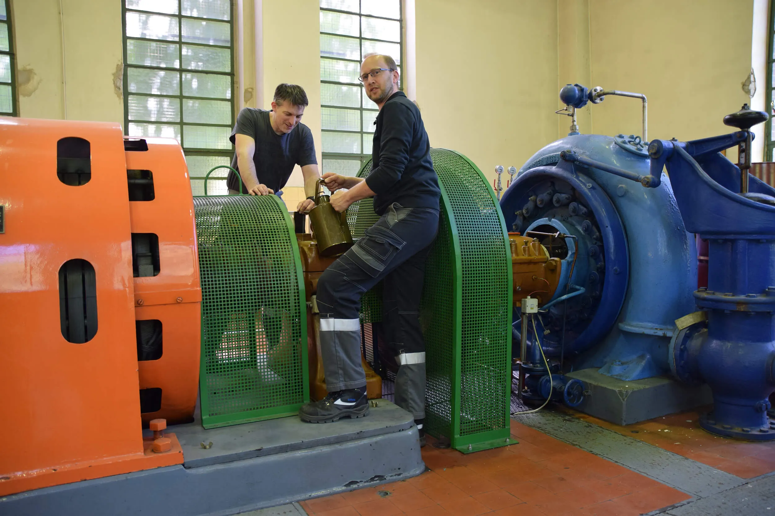 Zwei Techniker arbeiten an einer großen Maschine in einer Industriehalle, um Wartungsarbeiten durchzuführen.