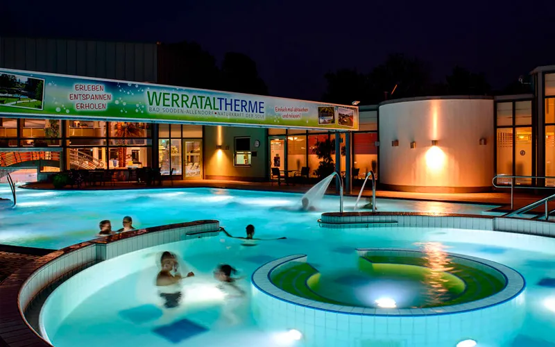 Beleuchteter Innenbereich der Werrataltherme mit schwimmenden Gästen in einem Pool bei Nacht.