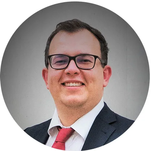Lächelnder Mann mit Brille, im Anzug, vor neutralem Hintergrund, Kreisformat.