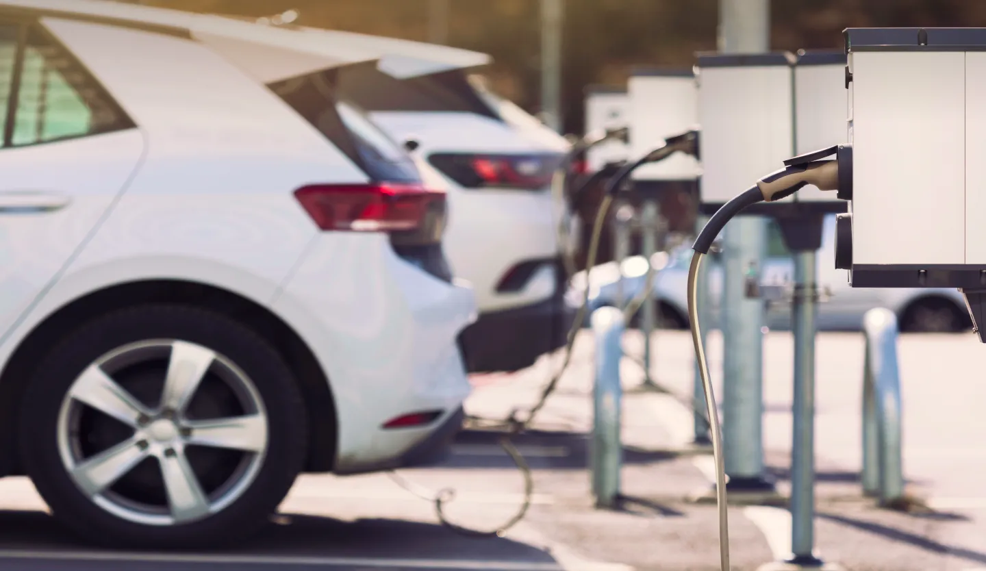 E-Ladestationen auf einem Parkplatz mit geparkten Elektrofahrzeugen im Hintergrund.
